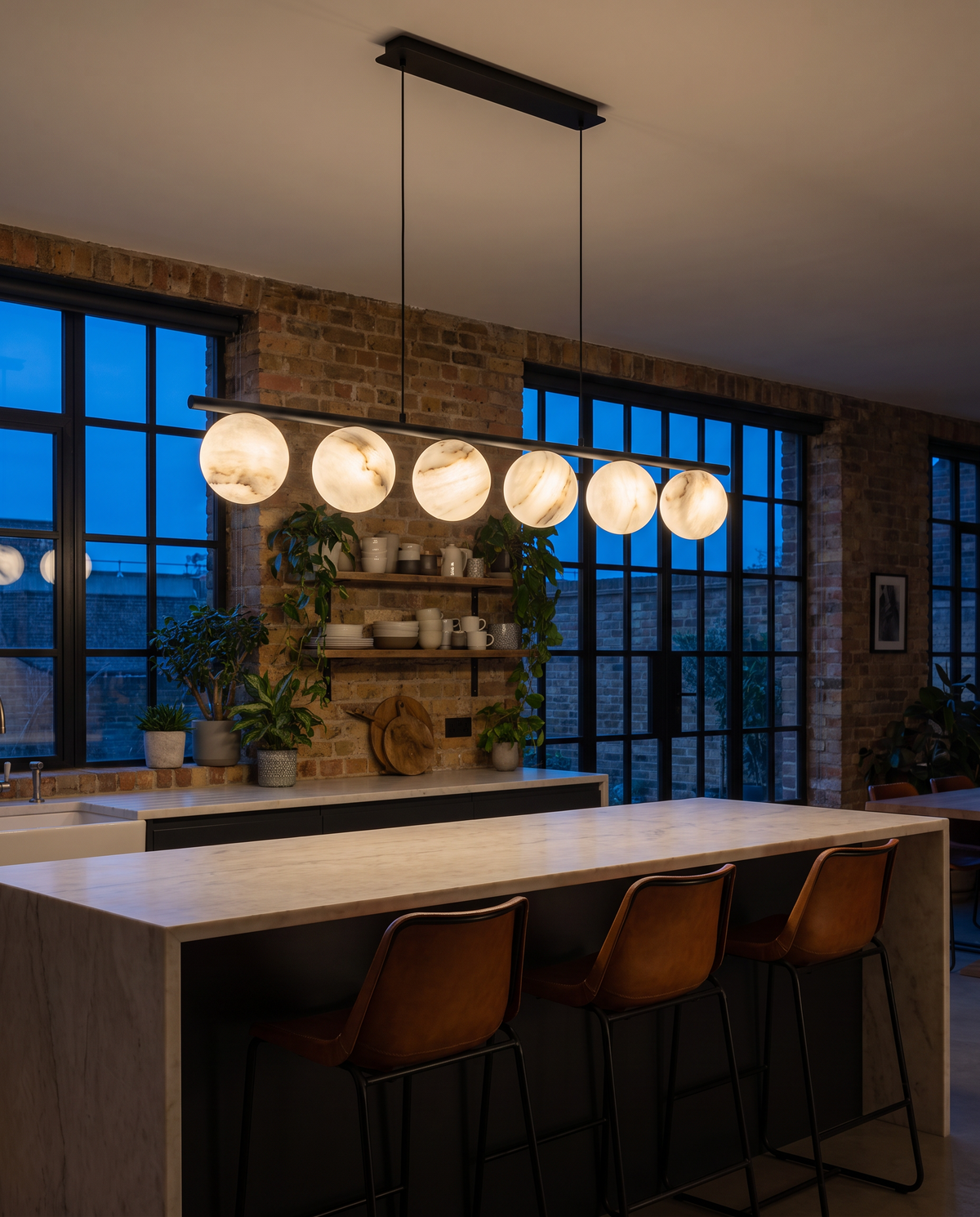 Battersea alabaster linear pendant in black glowing above a kitchen island in a brick warehouse kitchen